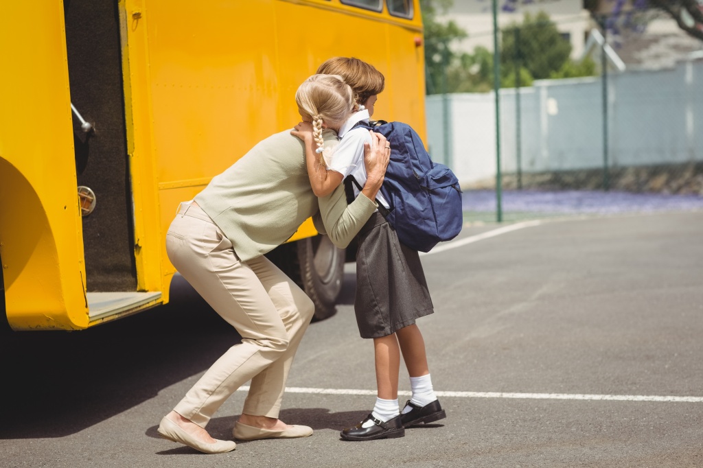 White mom hugging white child in front of school bus